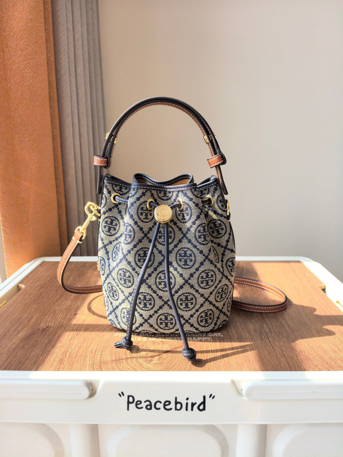 ToryBurch's new 1616A vintage water bucket bag features a classic TMonogram pattern fused with jacquard fabric, creating a charming and timeless style. This mini water bucket bag is adorned with delicate leather trim, a top handle, and a detachable diagon