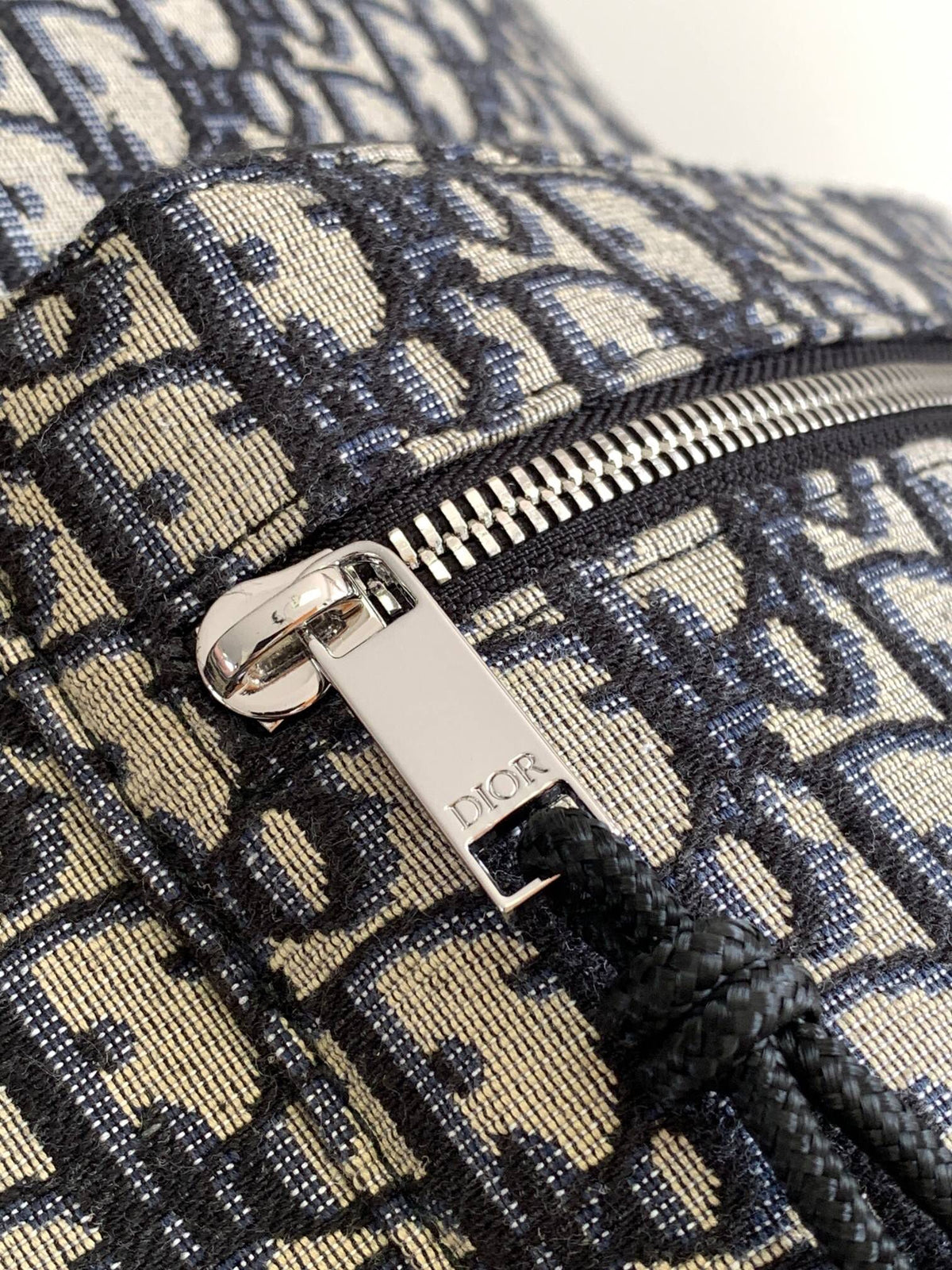 Under the small black lettering. This Rider backpack has a simple silhouette. The classic collegiate style is full of energy. Inspired by the Dior men's collection. Reinterpreted in beige and blue jacquard fabrics. Oblique print throughout. Continuing