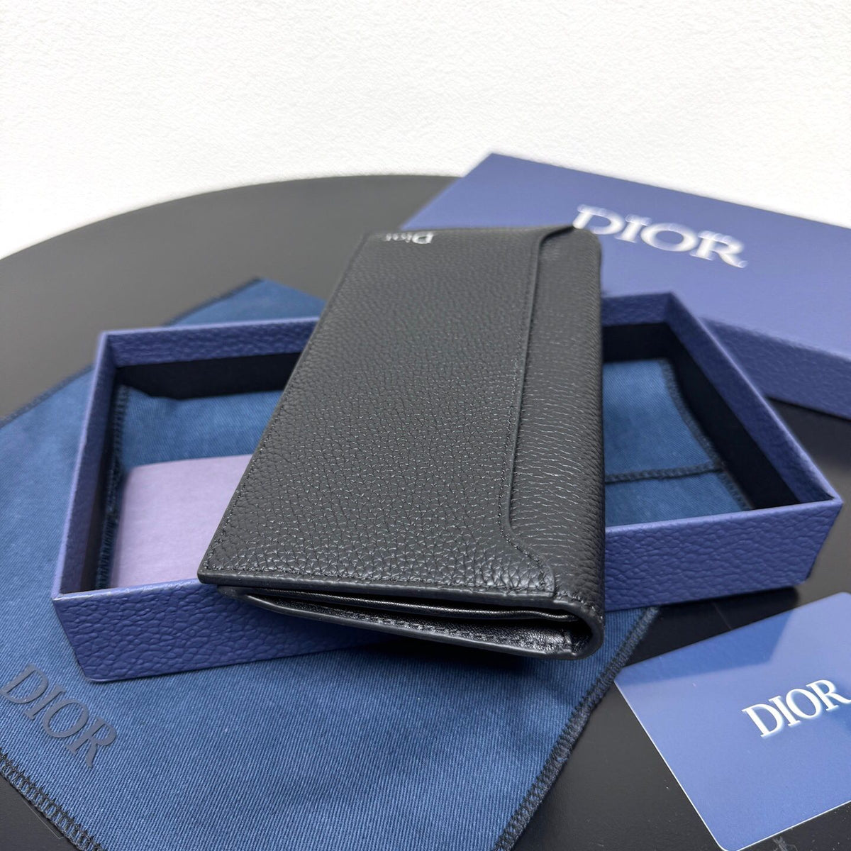 Stylish and functional, this vertical bi-fold wallet is crafted from black grained cow leather. Vertical bi-fold design. CD logo on front for added style. Features five cash compartments, 16 card slots and a zippered coin compartment. Long vertical design