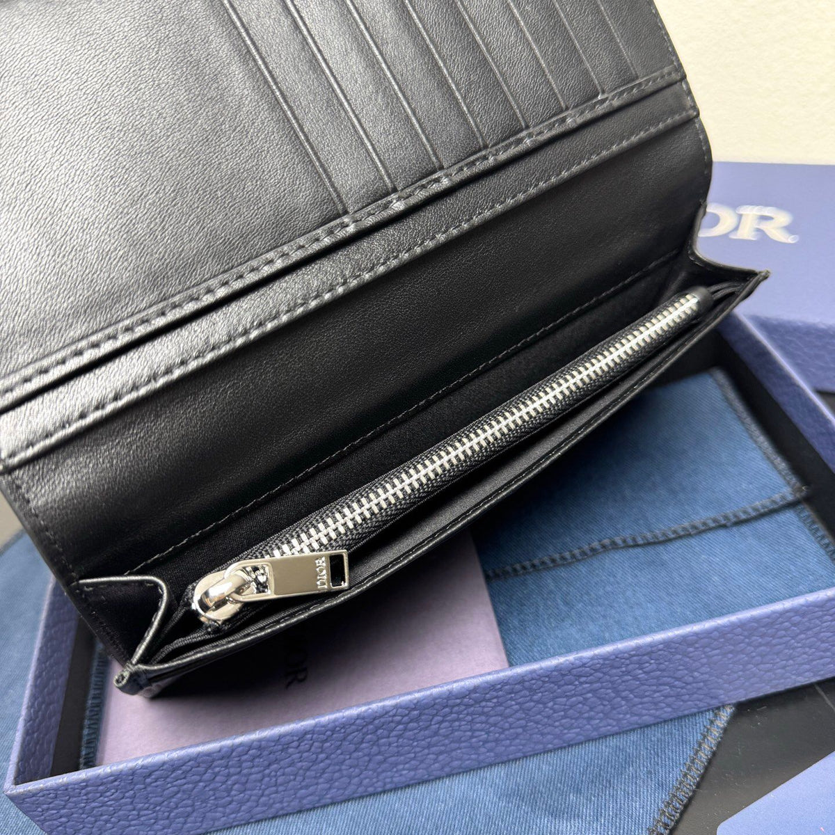 Stylish and functional, this vertical bi-fold wallet is crafted from black grained cow leather. Vertical bi-fold design. CD logo on front for added style. Features five cash compartments, 16 card slots and a zippered coin compartment. Long vertical design