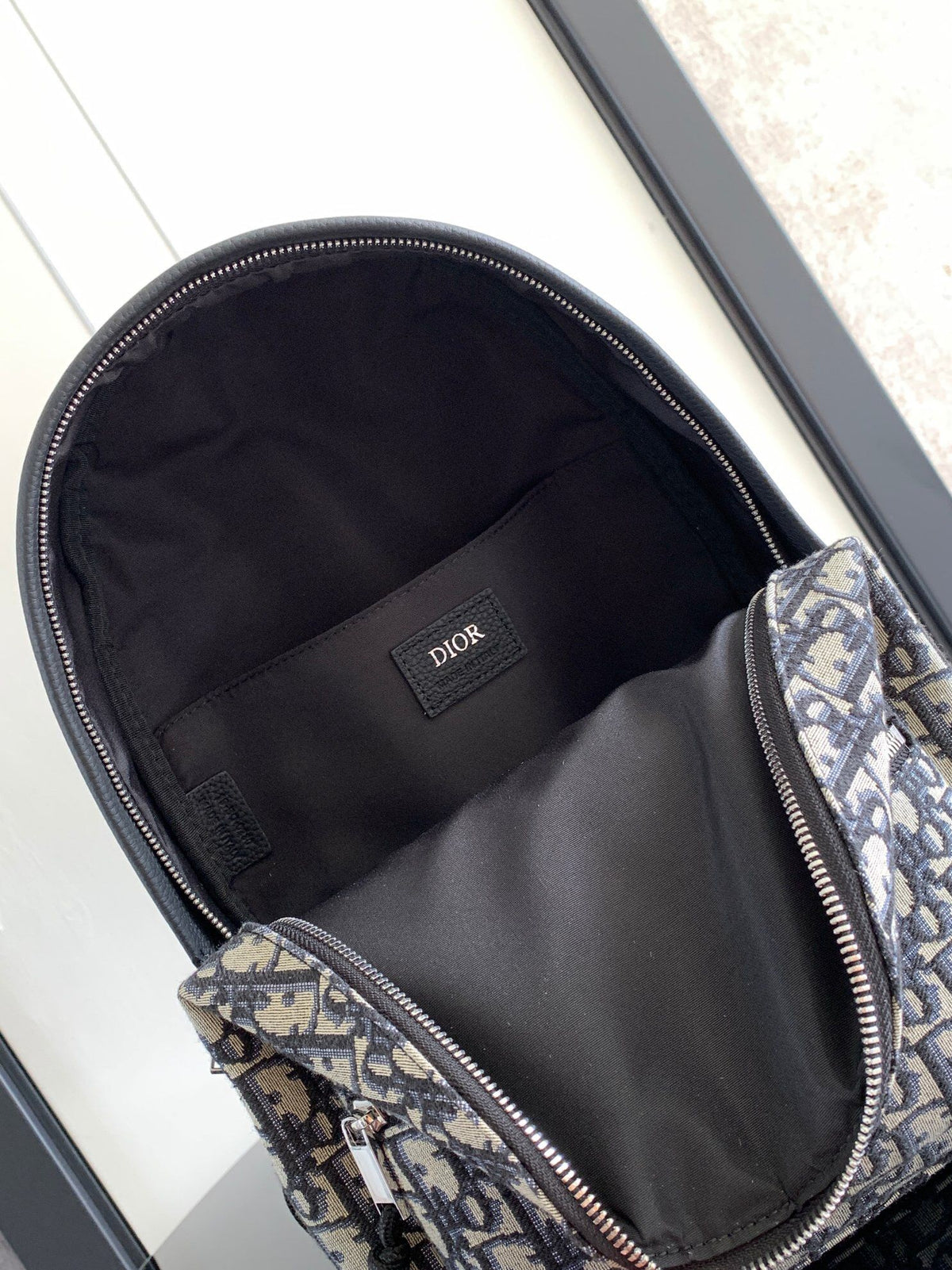 Under the small black lettering. This Rider backpack has a simple silhouette. The classic collegiate style is full of energy. Inspired by the Dior men's collection. Reinterpreted in beige and blue jacquard fabrics. Oblique print throughout. Continuing