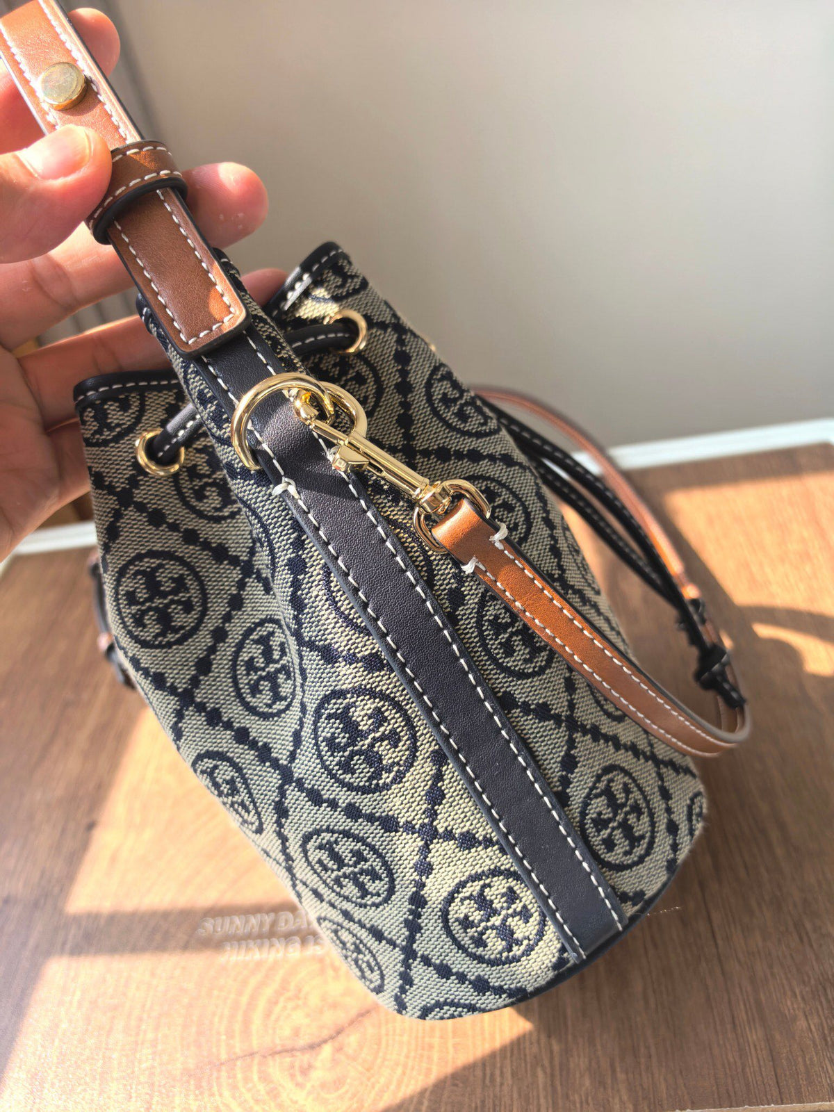 ToryBurch's new 1616A vintage water bucket bag features a classic TMonogram pattern fused with jacquard fabric, creating a charming and timeless style. This mini water bucket bag is adorned with delicate leather trim, a top handle, and a detachable diagon