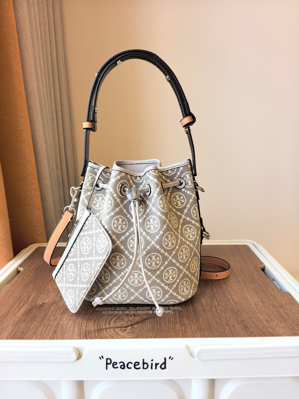ToryBurch's new 1615A vintage water bucket bag features a classic TMonogram pattern fused with jacquard fabric, creating a charming and timeless style. This bucket bag is adorned with delicate leather trim, a top handle, and a detachable diagonal strap