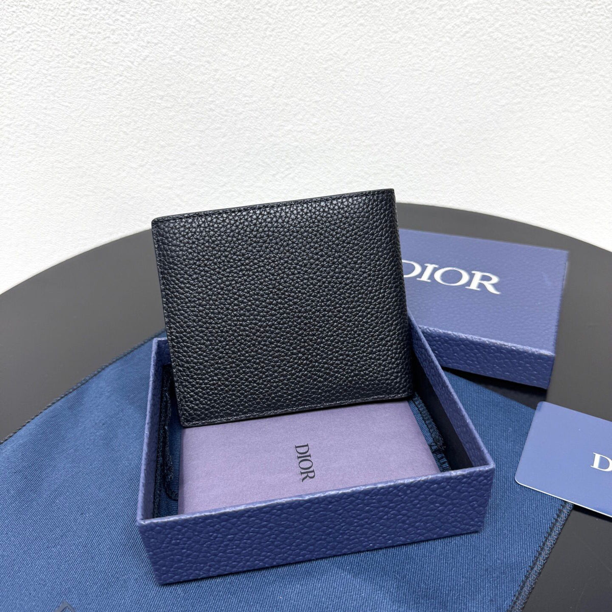 This bifold wallet is a compact accessory. Sophisticated and elegant. Crafted from grained calfskin. CD logo on the front. Features a double cash compartment on the interior. Two bill pockets and eight card slots. Bifold style fits easily into a pocket