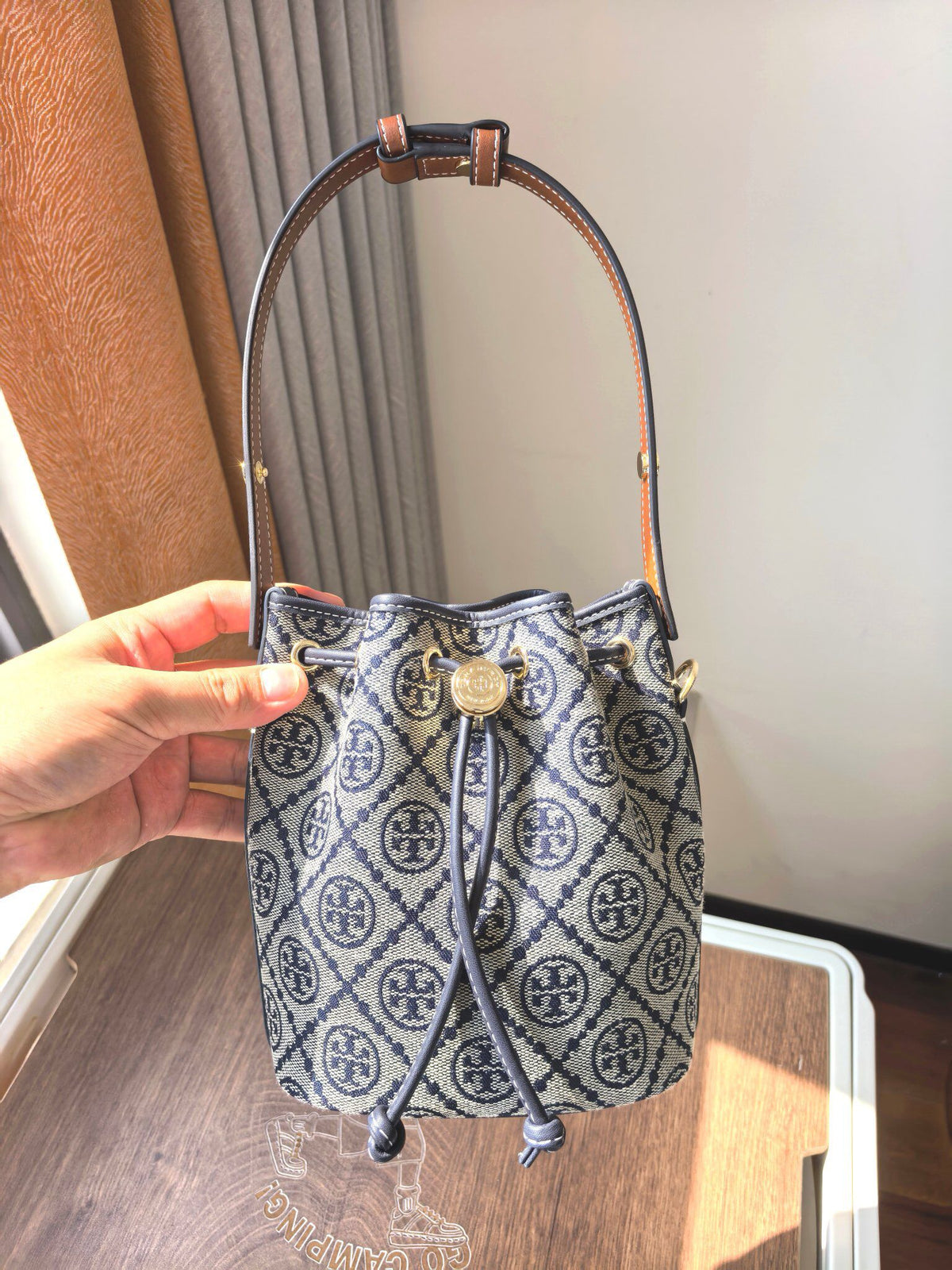 ToryBurch's new 1616A vintage water bucket bag features a classic TMonogram pattern fused with jacquard fabric, creating a charming and timeless style. This mini water bucket bag is adorned with delicate leather trim, a top handle, and a detachable diagon
