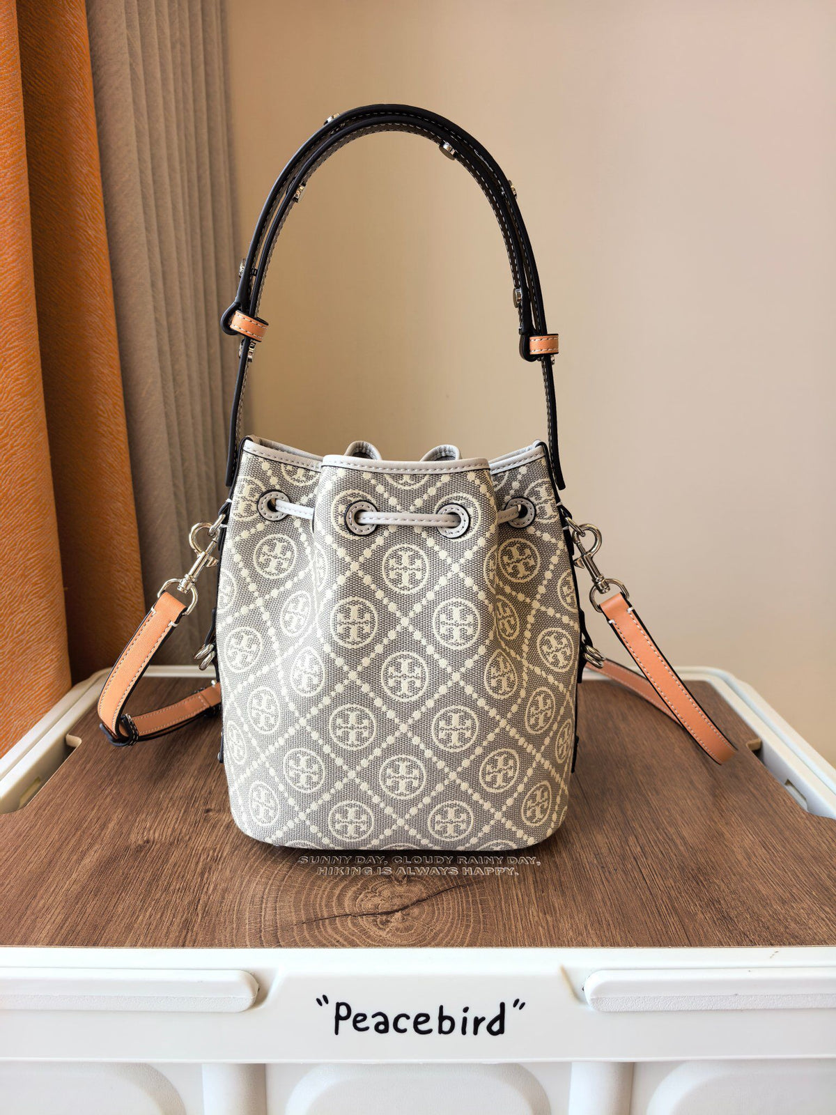 ToryBurch's new 1615A vintage water bucket bag features a classic TMonogram pattern fused with jacquard fabric, creating a charming and timeless style. This bucket bag is adorned with delicate leather trim, a top handle, and a detachable diagonal strap