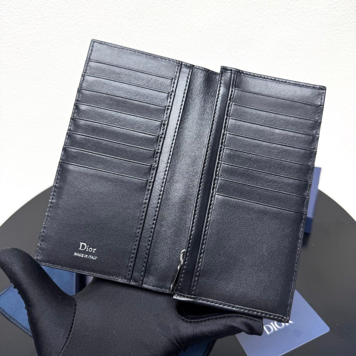 Stylish and functional, this vertical bi-fold wallet is crafted from black grained cow leather. Vertical bi-fold design. CD logo on front for added style. Features five cash compartments, 16 card slots and a zippered coin compartment. Long vertical design