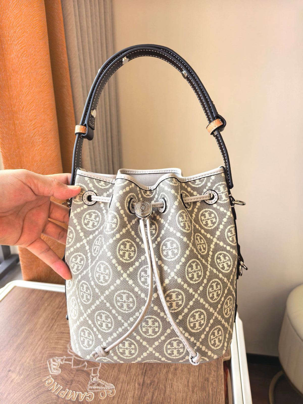 ToryBurch's new 1615A vintage water bucket bag features a classic TMonogram pattern fused with jacquard fabric, creating a charming and timeless style. This bucket bag is adorned with delicate leather trim, a top handle, and a detachable diagonal strap