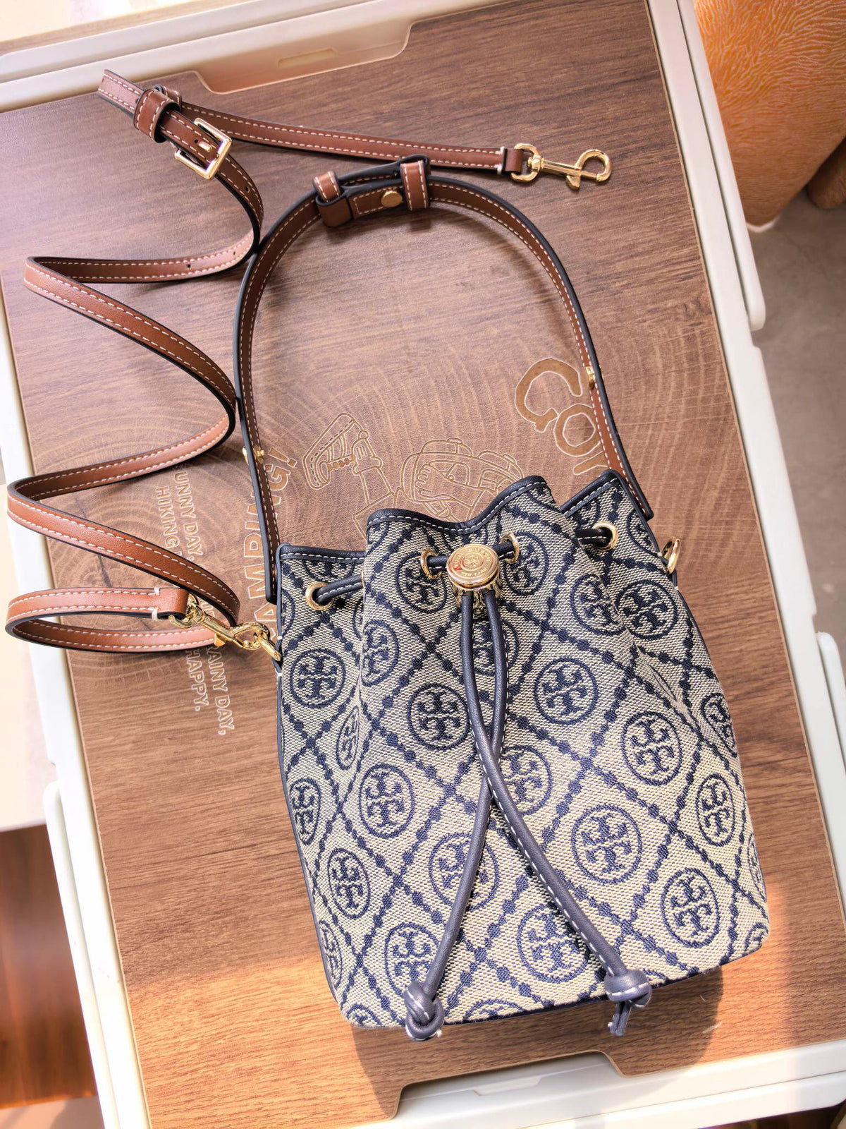 ToryBurch's new 1616A vintage water bucket bag features a classic TMonogram pattern fused with jacquard fabric, creating a charming and timeless style. This mini water bucket bag is adorned with delicate leather trim, a top handle, and a detachable diagon